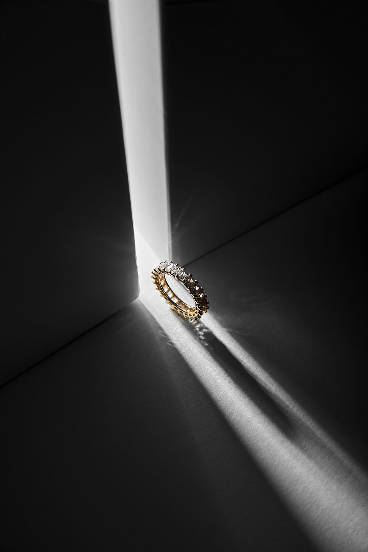 render of a yellow gold eternity band set with emerald cut diamonds, lit by a single hard shaft of light
