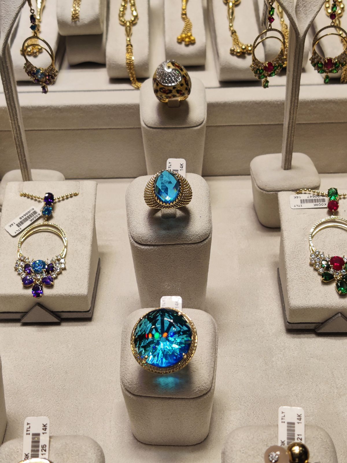 retail showcase of 14k gemstone rings and pendants on suede stands, each carrying a barcoded stock ticket